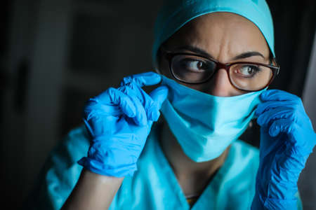 Close up shot of a woman doctor adjusting her surgical mask and glasses, in natural light.の写真素材