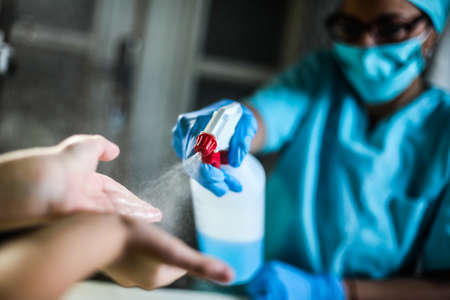 Woman doctor holds a disinfectant dispenser and sprays on kid's hands.の写真素材