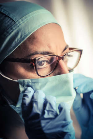 Close up shot of a woman doctor adjusting her surgical mask and glasses, in natural light.の写真素材