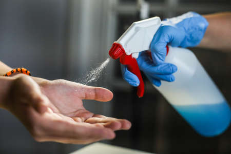 Doctor holds a disinfectant dispenser and sprays on kid's hands.の写真素材