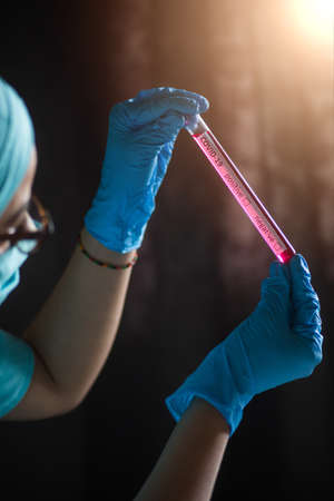 Conceptual photograph of a doctor holding and looking at a test tube while testing samples for...