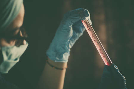 Conceptual photograph of a doctor holding and looking at a test tube while testing samples for presence of coronavirus (COVID-19).の写真素材