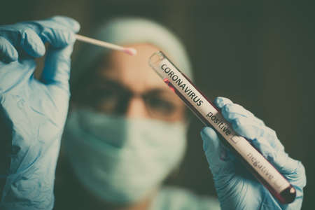Conceptual photograph of a doctor holding and looking at a test tube while testing samples for presence of coronavirus (COVID-19).の写真素材