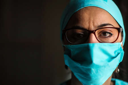 Close up shot of a woman doctor wearing a surgical mask and glasses, in natural light.