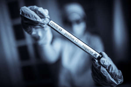 Conceptual photograph of a doctor's hands holding and looking at a test tube while with negative samples for the presence of coronavirus (COVID-19).の写真素材