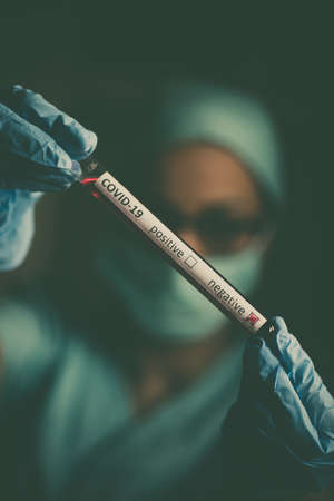 Conceptual photograph of a doctor's hands holding and looking at a test tube while with negative samples for the presence of coronavirus (COVID-19).の写真素材