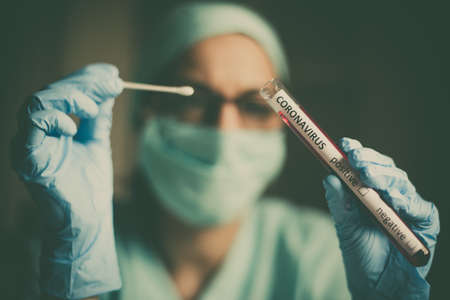 Conceptual photograph of a doctor holding and looking at a test tube while testing samples for presence of coronavirus (COVID-19).の写真素材