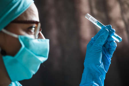 Conceptual photograph of a doctor holding and looking at a test tube while testing samples for...