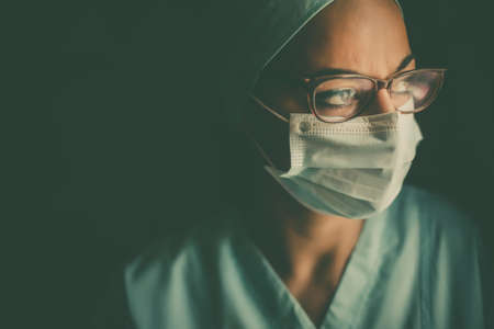Color portrait of a young female medic arranging her gloves, wearing a mask and glasses, illustration for the coronavirus Covid-19 pandemic.の写真素材
