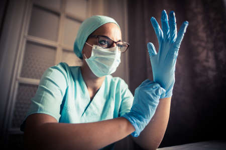 Portrait of a young woman talking on the mobile phone while wearing a mask, indoor, by a window.の写真素材