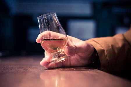 Color close up shot a hand holding a Glencairn whisky glass on a wooden table, with shallow depth of field.の写真素材