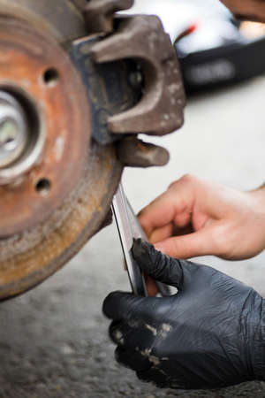 Close up shot of a mechanic working at a car worn and rusty brake disk and caliper.の写真素材