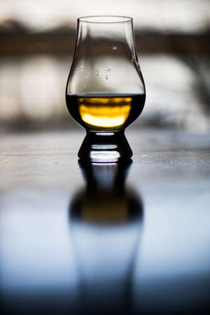 Color close up shot a hand holding a Glencairn whisky glass on a wooden table, with shallow depth of field.の写真素材