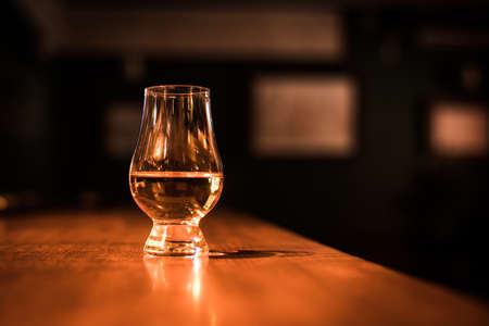 Color close up shot a hand holding a Glencairn whisky glass on a wooden table, with shallow depth of field.の写真素材