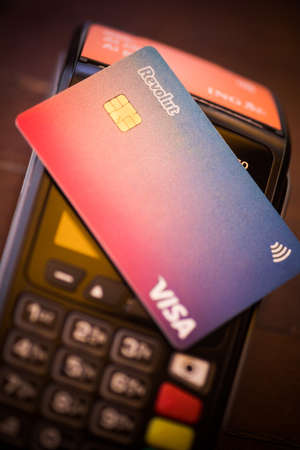 Bucharest, ROMANIA - May 17, 2021: Illustrative editorial concept image of a person holding a Revolut VISA card near a POS terminal.のeditorial素材