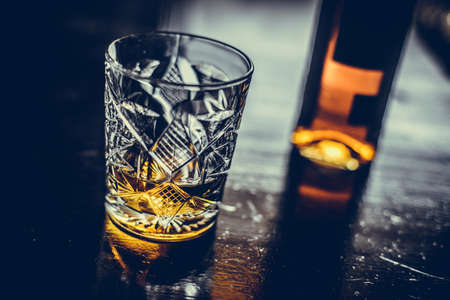 Close up shot of a whisky glass and a bottle on a wooden surface.の写真素材