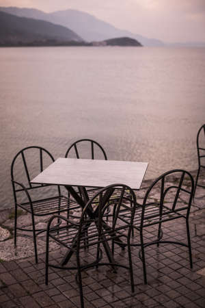 Color image of empty chairs and tables at an open air terrace, near a lake.