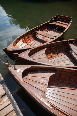 Close up shot of three wooden boats on a lake, by a pier.