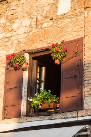Close up shot of an open window with shades and flowers, on an old brick building.の写真素材