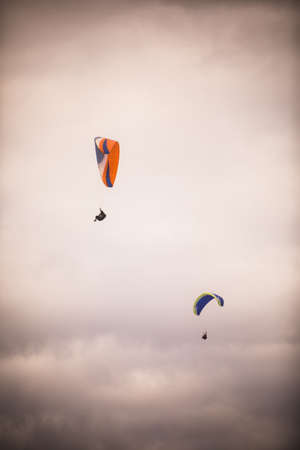 Image of some paragliders flying, against a gray cloudy sky.の写真素材