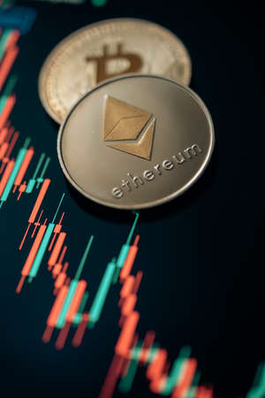 Stack or heap of silver Bitcoin and Ethereum cryptocurrency with candle stick graph chart and...