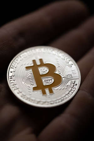 Close up shot of hand holding a silver bitcoin digital cryptocurrency.