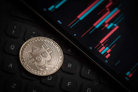 Silver Bitcoin cryptocurrency coin with candle stick graph chart, laptop keyboard, and digital background.の写真素材