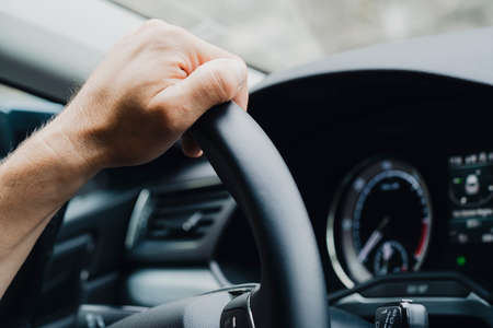 Close up shot of male hands on a car's steering wheel.