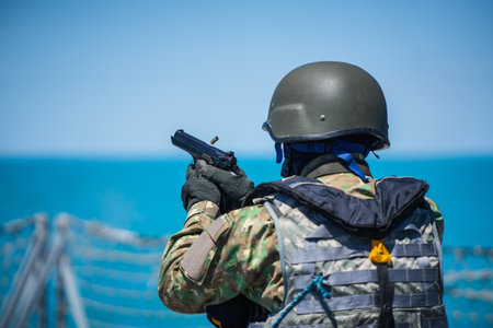 Color image of a soldier dressed in camouflage uniform firing a pistol gun at a target.
