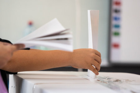 A person inserts a ballot in a box while voting at a polling station during elections.の写真素材
