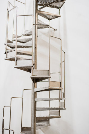 Fragment of modern metal spiral staircase against a white wall.