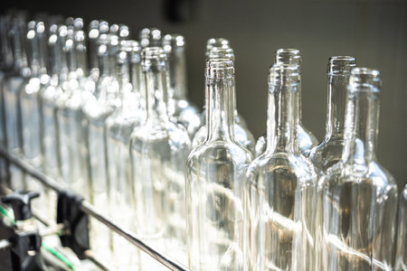 Line of empty glass bottles on a conveyor belt, at a drink bottling factory.
