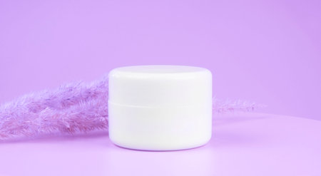 a white glass jar for moisturizing cream with a gold lid on purple or lilac background. Mockup for branding product packaging.の写真素材
