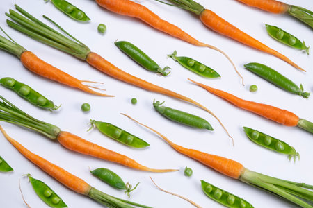 background of young carrots and green peas on a white background, fresh vegetables, the concept of proper healthy nutritionの写真素材