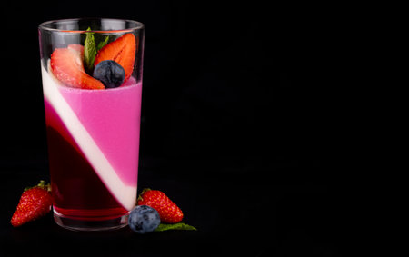 Fruit jelly with strawberries and blueberries in a glass on a black background template for inserting text, a beautiful dessertの写真素材