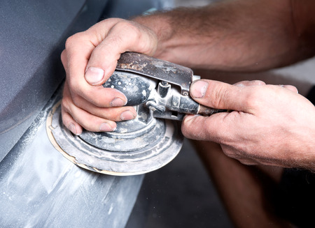 Worker is sanding filler with air sander in auto body shop