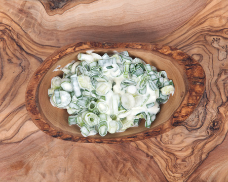Organic green onion scallion salad with sour cream in bowl on olive wood cutting boardの写真素材