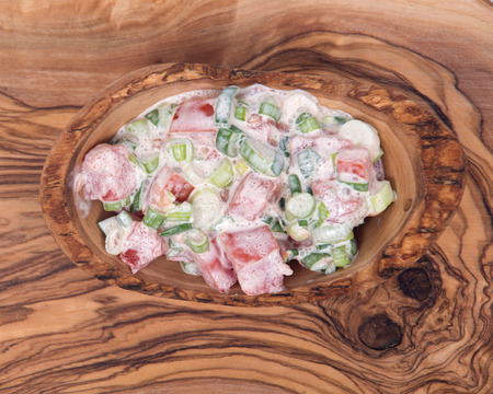Organic tomato and green onion scallion salad with sour cream in bowl on olive wood cutting boardの写真素材