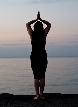 Young active woman practicing yoga on the beach at sunriseの写真素材