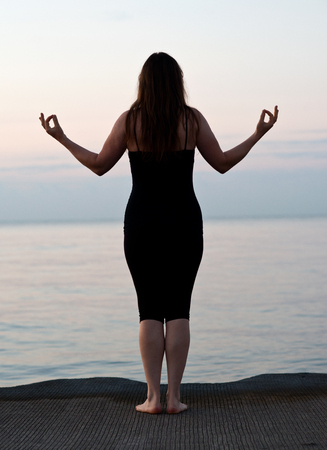 Young active woman practicing yoga on the beach at sunriseの写真素材