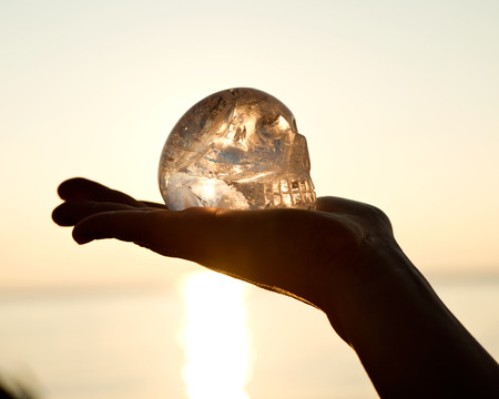 Clear quartz skull on the woman`s open palm in front of  the rising sunの写真素材