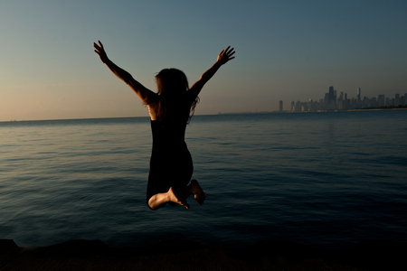 Happy woman jumping near by Lake Michigan at sunrise with downtown of Chicago in the backの写真素材