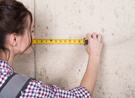 Young woman working with measuring tape in house under reconstructionの写真素材