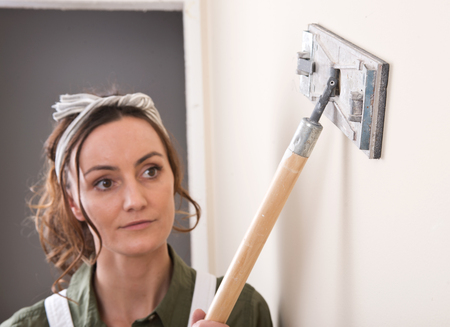 Young woman is sanding wall with pole sander before painting in house under remodelingの写真素材