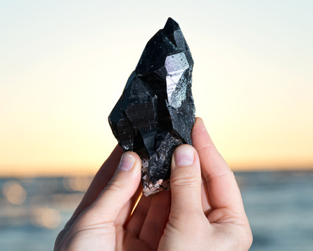 Woman holding Morion Smokey Quartz with Chlorite  in her hand at sunrise in front of the lake.の写真素材