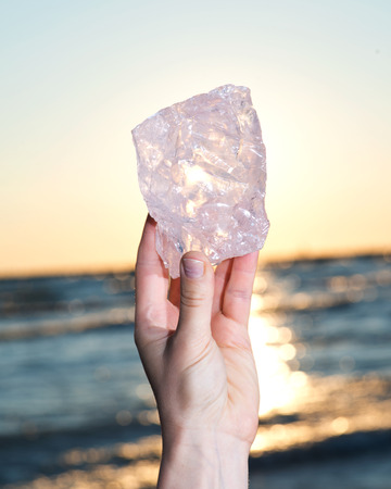 Woman's hand holding gem grade rough Rose Quartz chunk from Madagascar  in front of the lake at sunriseの写真素材