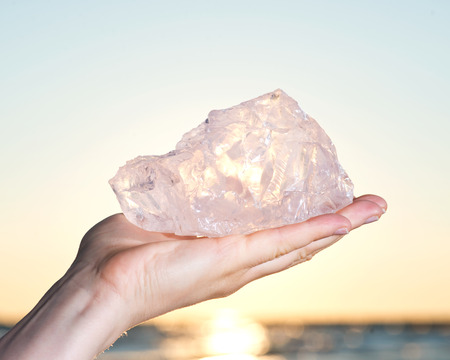 Woman's hand holding gem grade rough Rose Quartz chunk from Madagascar  in front of the lake at sunriseの写真素材