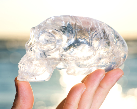 Woman's hand holding Quartz Carved Elongated Mayan Alien Crystal Skull at the sunrise in front of the lake.の写真素材