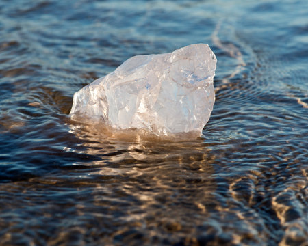 Gem grade rough Rose Quartz chunk from Madagascar lying on wet sand  in front of the lake at...