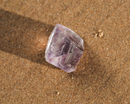 Purple Fluorite Natural Octahedron Crystal on the beach at sunrise.